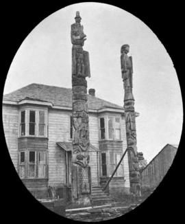 Two totem poles in front of two-story house