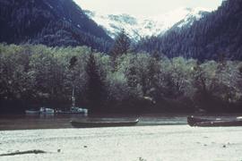 Canoes on shore and boats in river, near mountains