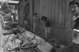 [Isaac rakes debris outside long house]