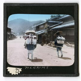 Two people with packs walking down road near buildings