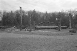 [Canoe log, totem poles, and long house]