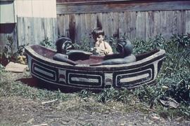Boy next to carving of canoe and two figures